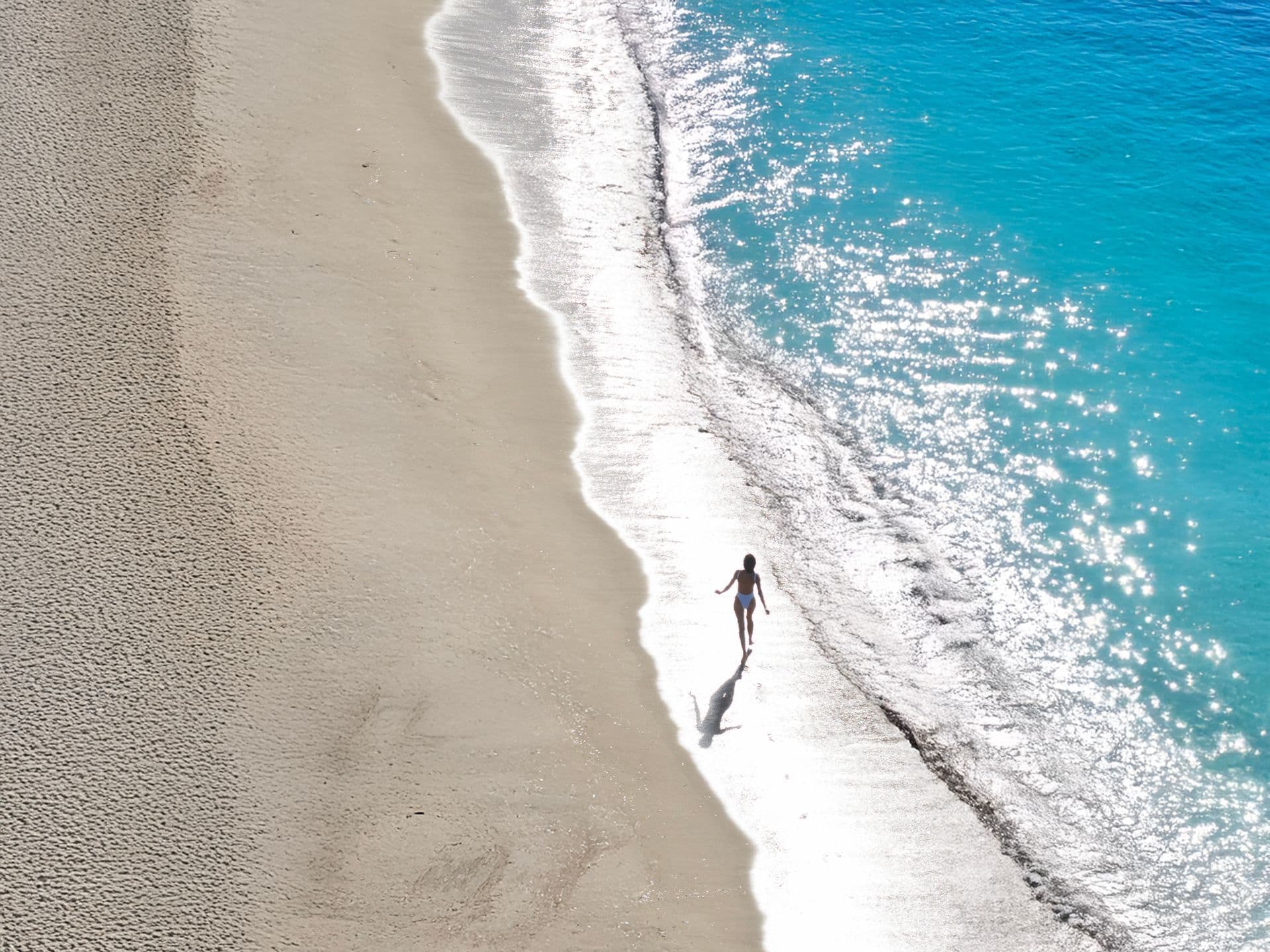  Female walking on the wet sand of a beach in Paros, one of the alternatively quiet Greek islands