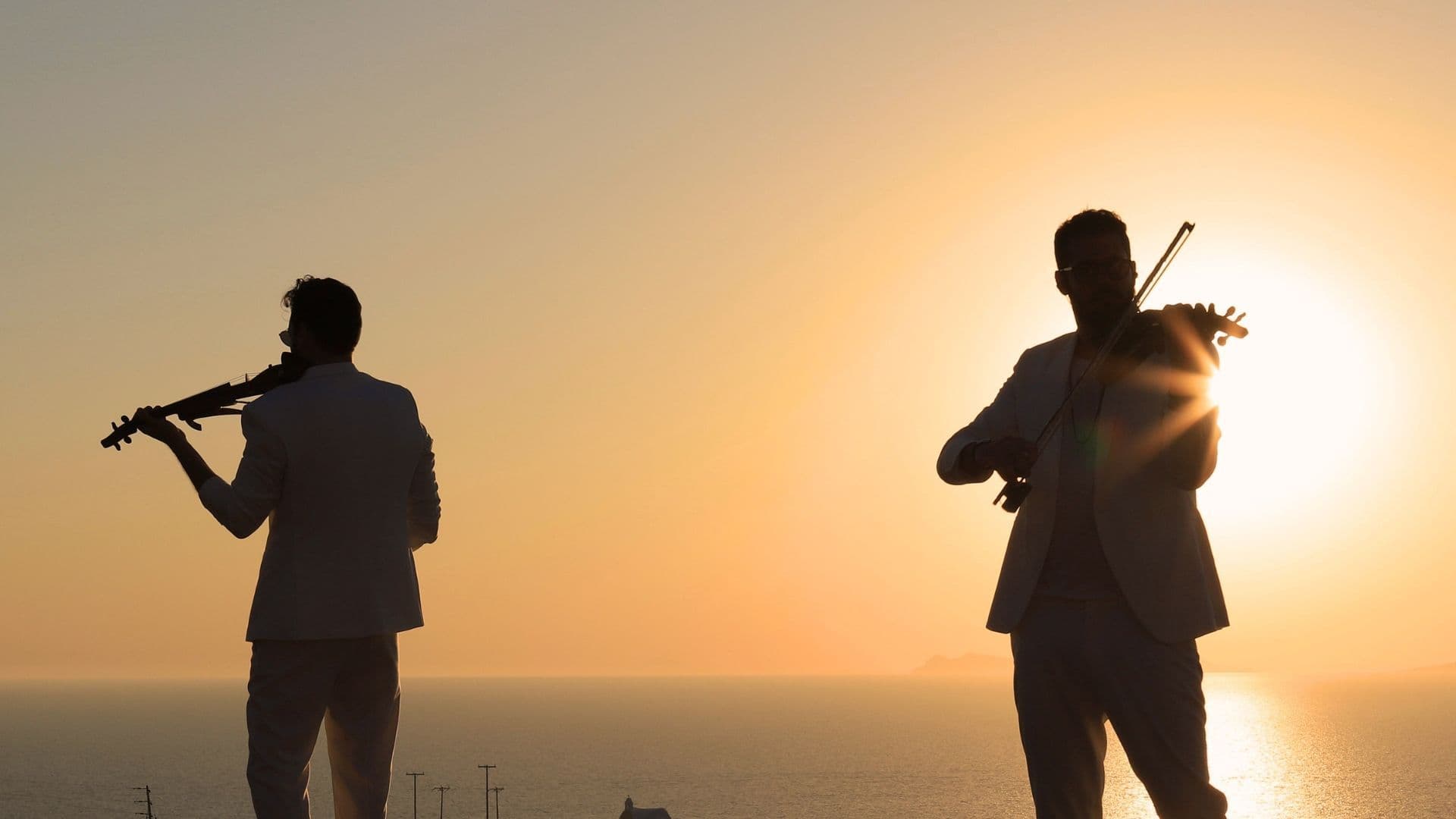 Duo Violins pictured against the sunset at Pacman Sunset Restaurant within Andronis Arcadia, part of the live music Santorini events by ANDRONIS.