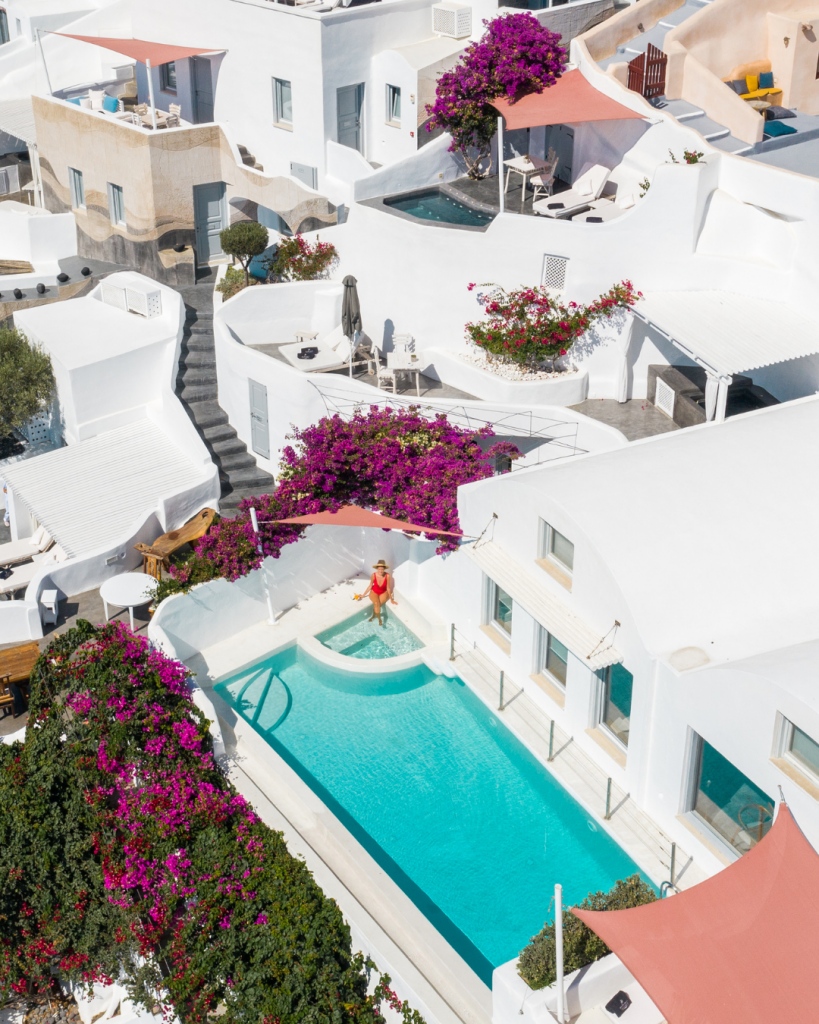 Aerial view of Infinity Luxury Suite in Santorini. A girl in red swimsuit sitting in the a hot tub in the private balcony
