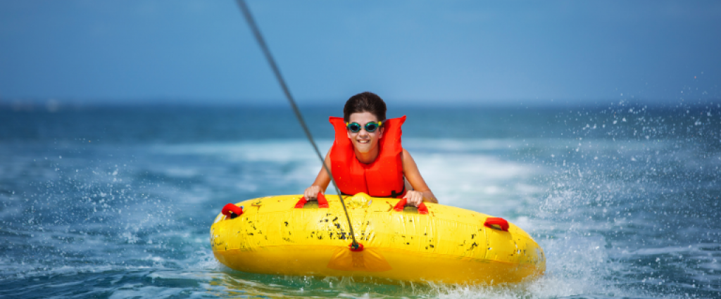 A kid in a life vest water tubing an yellow plastic boat