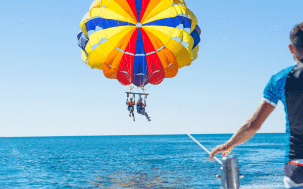 2 people parasailing above the sea, hanging from a colourful balloon