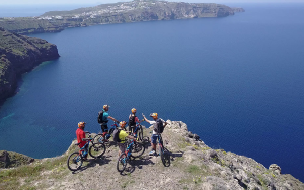 4 personas en bicicletas eléctricas de montaña, admirando la vista de Santorini