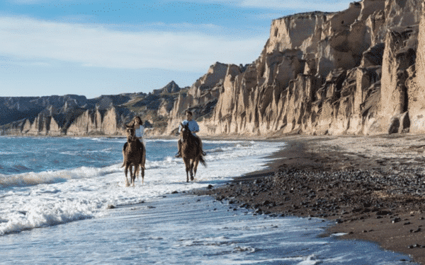 2 pessoas a montar a cavalo na praia em Santorini