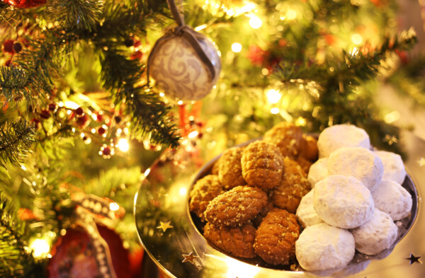 a plate full of Kourabiedes and melomakarona, greek traditional christmas sweets, next to a Christmas tree