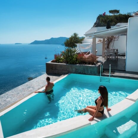 Guestσ at the edge of the infinity pool and volcano view from the terrace of one of Andronis three Santorini adults-only hotels in Oia