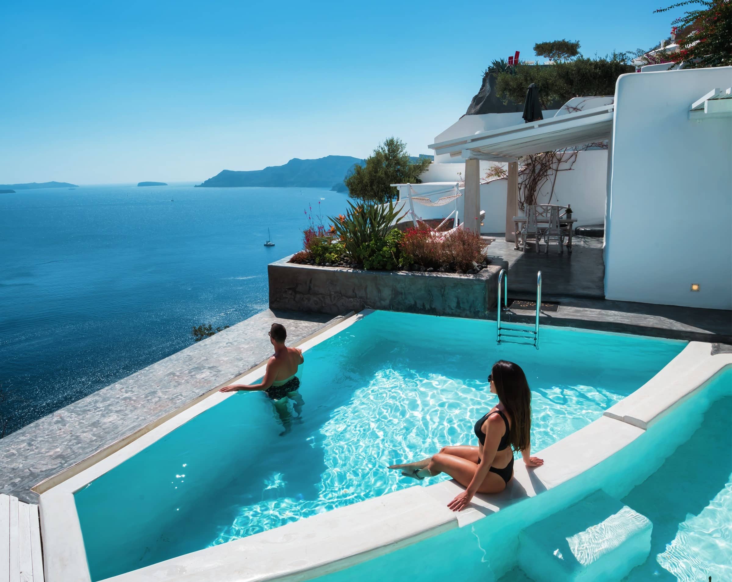 Guestσ at the edge of the infinity pool and volcano view from the terrace of one of Andronis three Santorini adults-only hotels in Oia